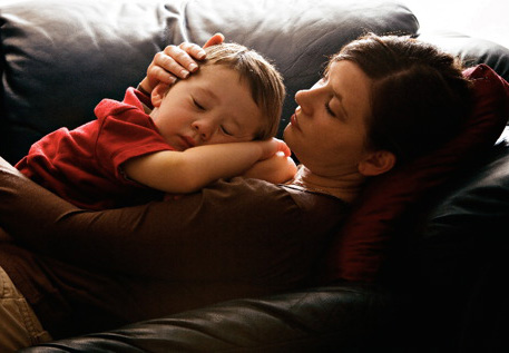 A child and his mother sleeping on the couch.